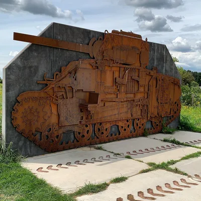 Rusted steel cutaway relief of a Sherman tank mounted on a concrete wall at Meinerswijk, Arnhem, with tank track marks set into the paving in front