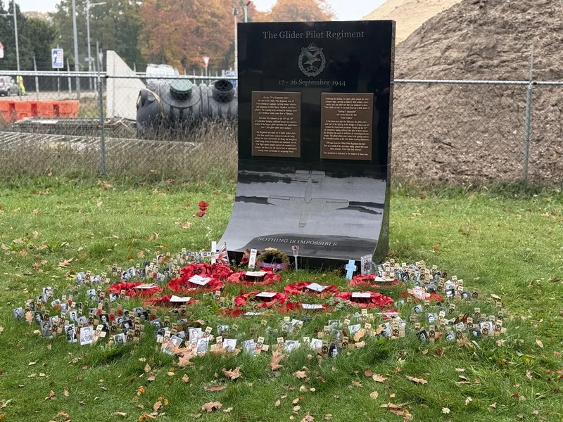 The black stone Glider Pilot Regiment memorial at Wolfheze, its base surrounded by poppy wreaths and small wooden crosses carrying photographs of glider pilots.