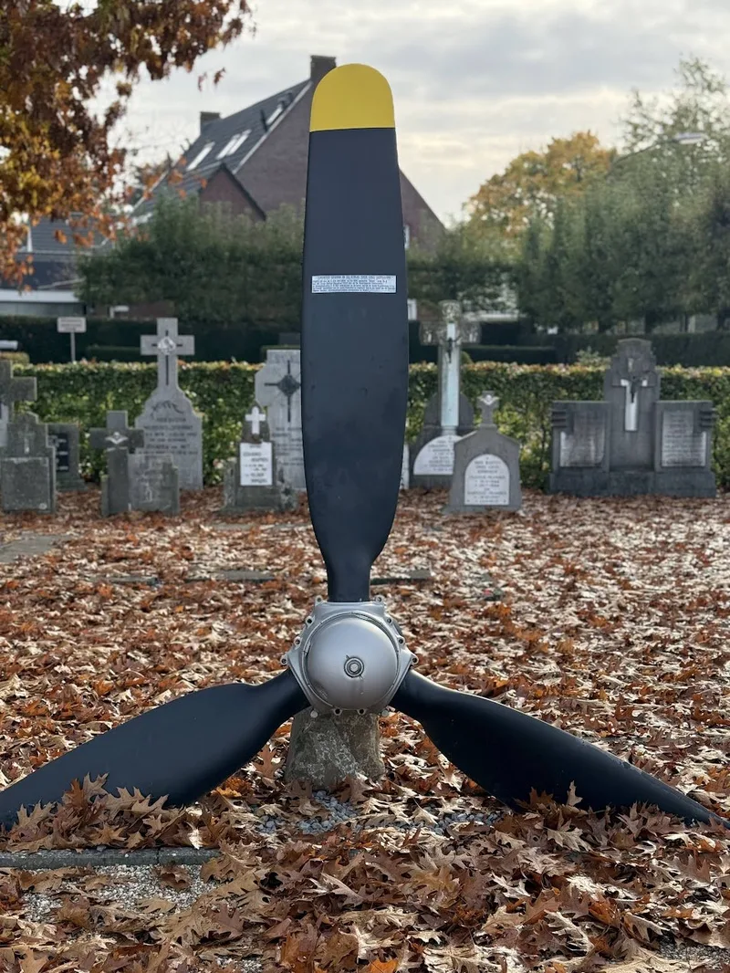 The Sonya's propeller standing upright among autumn leaves in the cemetery at Erp, with gravestones behind it