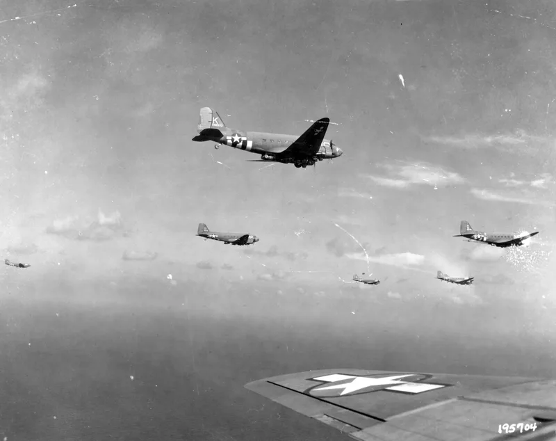 Black and white photo of C-47 Dakotas flying in formation, seen from the wing of another C-47